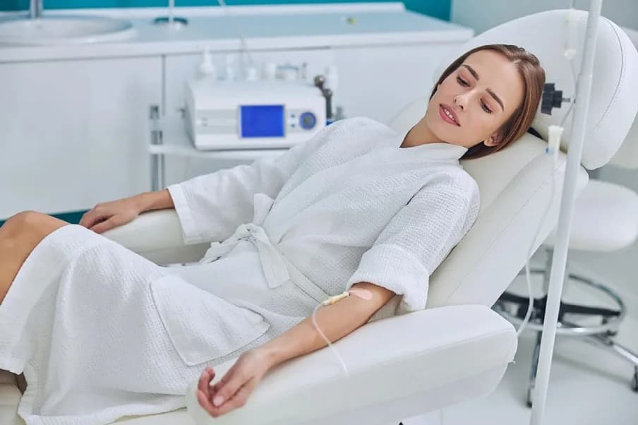 A woman resting in a treatment chair with an IV line secured to her arm